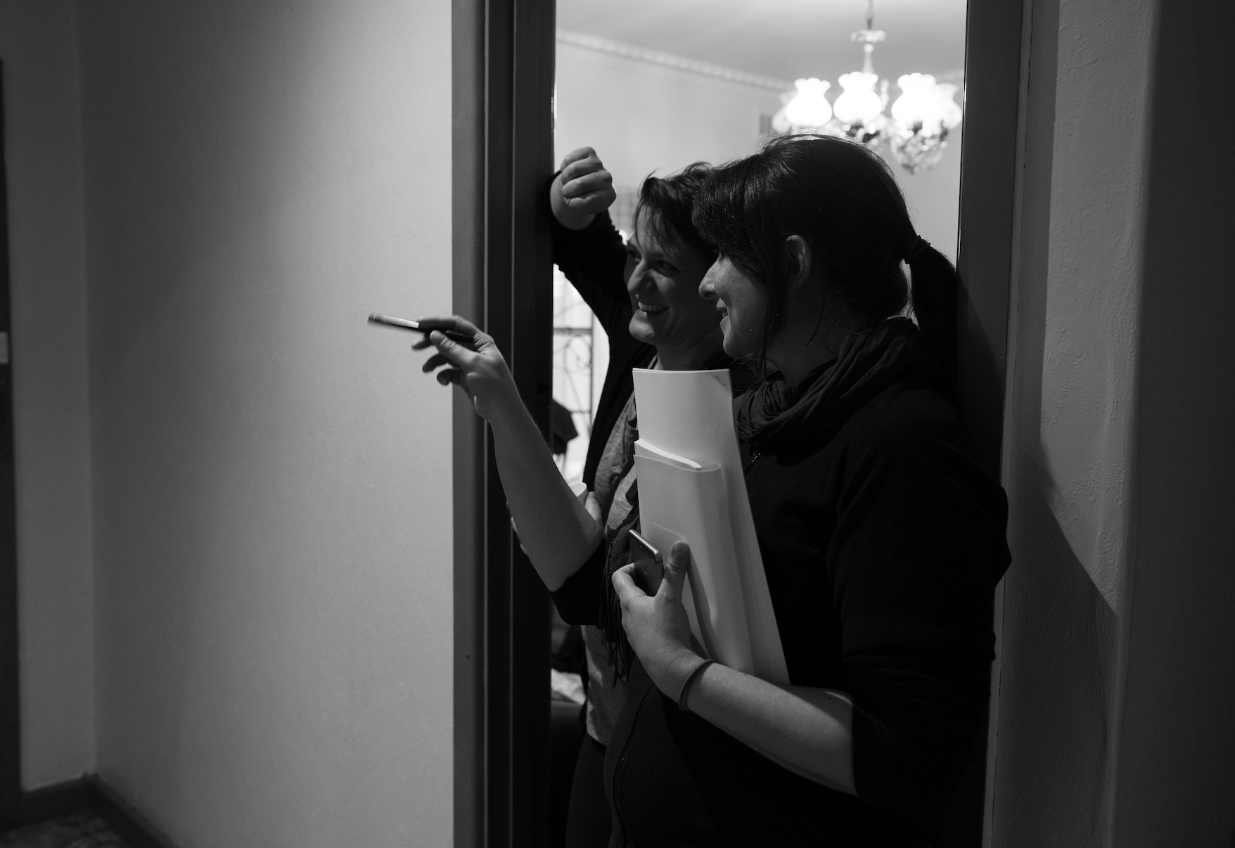 A black and white image of two women looking to the left. Natalia is holding papers and pointing to something outside of the frame.